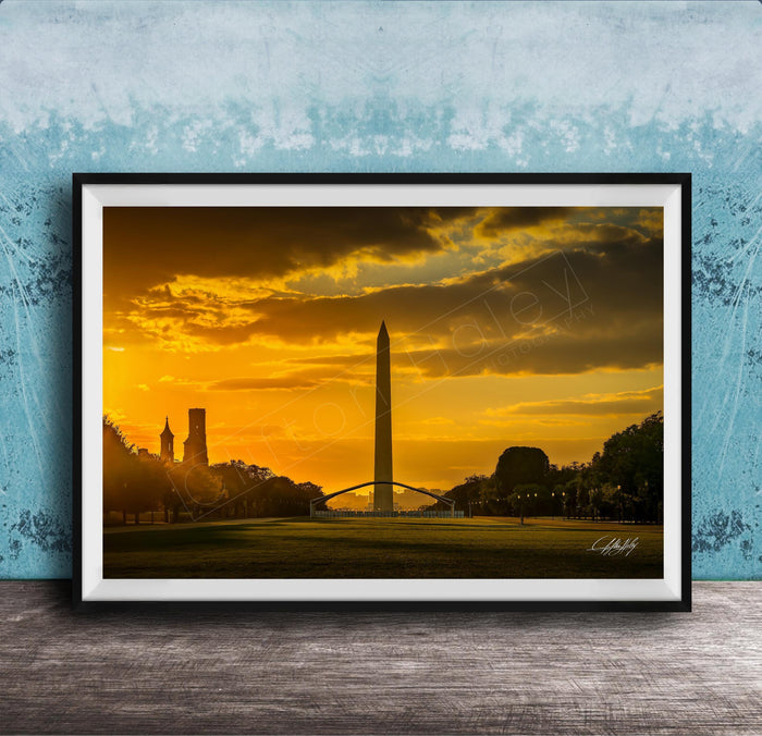 the Washington Monument at sunset, with the tall obelisk silhouetted against a vibrant orange and yellow sky.