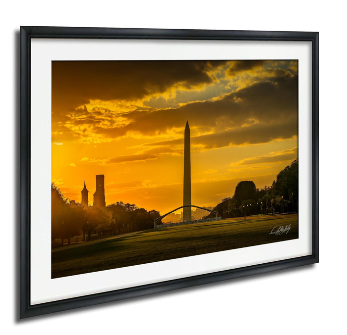 a cityscape at sunset, with the Washington Monument and other buildings silhouetted against a vibrant orange sky.