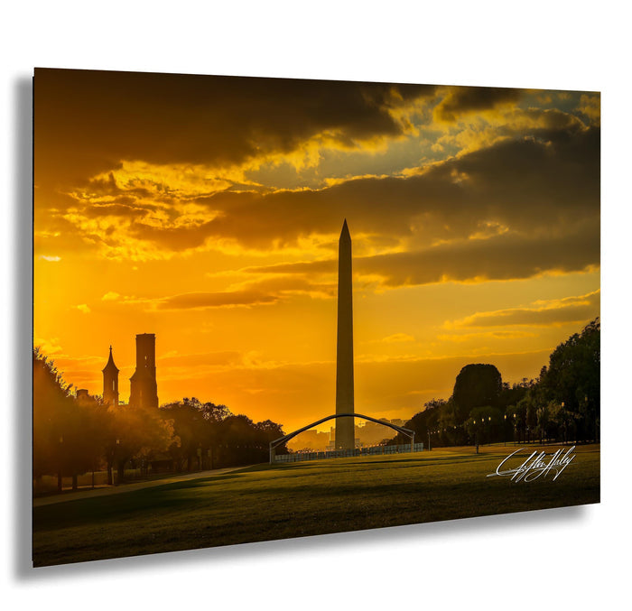 a serene sunset over a park, with the Washington Monument and other buildings silhouetted against the vibrant orange sky.
