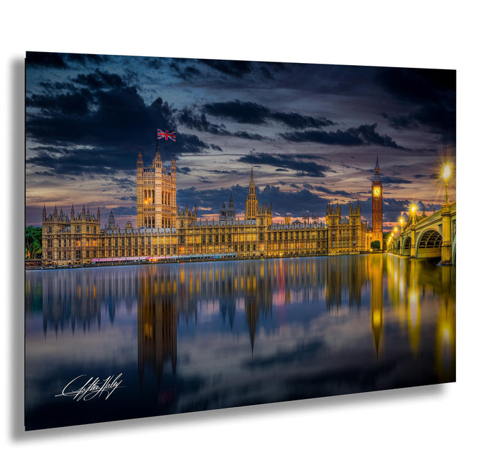 a city skyline at night, with the iconic Big Ben clock tower and other historic buildings illuminated against a dark sky. The calm water in the foreground reflects the cityscape, creating a serene and picturesque scene.