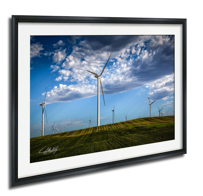 A framed photograph depicting a field with multiple wind turbines against a blue sky with clouds.