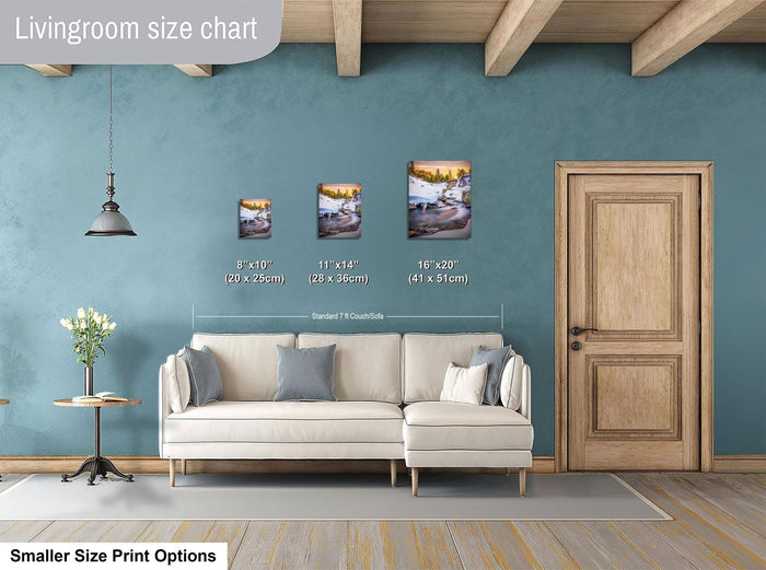 a living room with a white sofa and a wooden door. There are three framed pictures of different sizes displayed on the wall above the sofa.