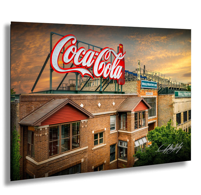 A large Coca-Cola sign is displayed on top of a brick building, with a stadium and other buildings visible in the background.