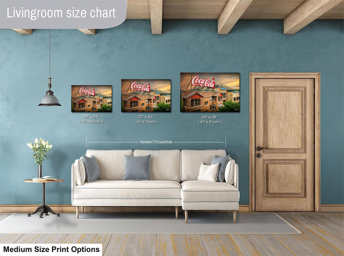 a living room with a white sofa and a wooden door. Above the sofa, there are three framed pictures of a building, each with a different size and resolution. The wall behind the sofa has a blue color, and there is a lamp hanging from the ceiling. The image also includes text that provides information about the living room size chart and medium size print options.