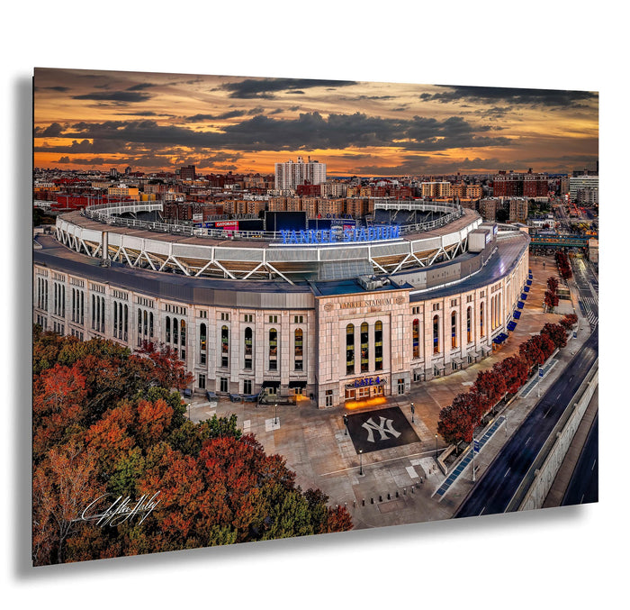 a large, circular stadium with a distinctive New York Yankees logo, surrounded by a cityscape and a colorful sunset sky.