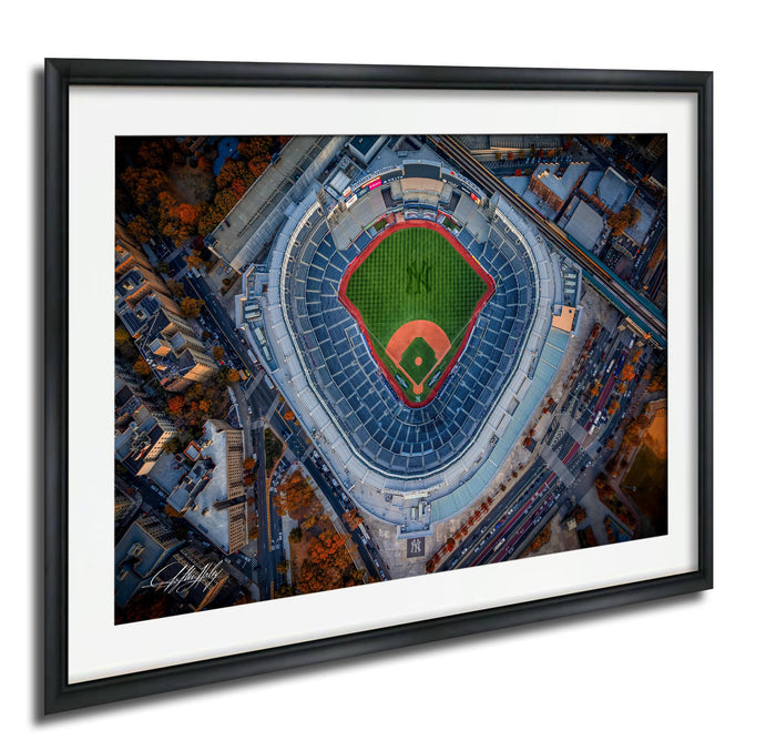 An aerial view of a baseball stadium with a green field and red diamond, surrounded by a cityscape with buildings and trees.
