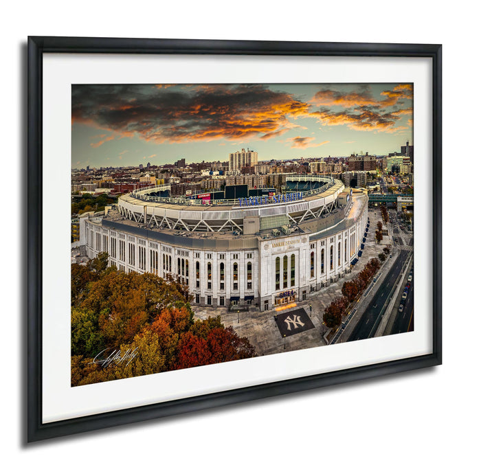 The image is a framed photograph of a large stadium, likely a sports stadium, with a city skyline in the background. The photograph is taken from an aerial perspective, showcasing the stadium and surrounding urban landscape.