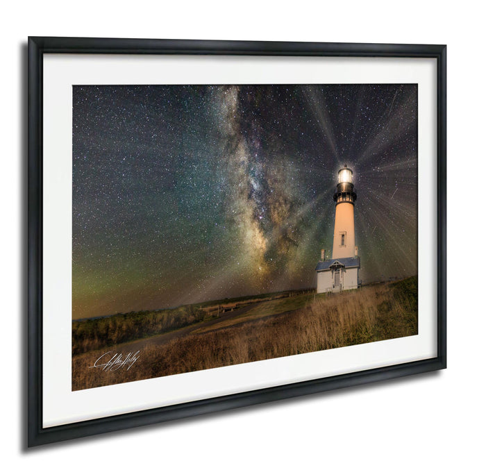 A framed photograph depicting a lighthouse standing in a field at night, with a starry sky and a glowing milky way galaxy in the background.