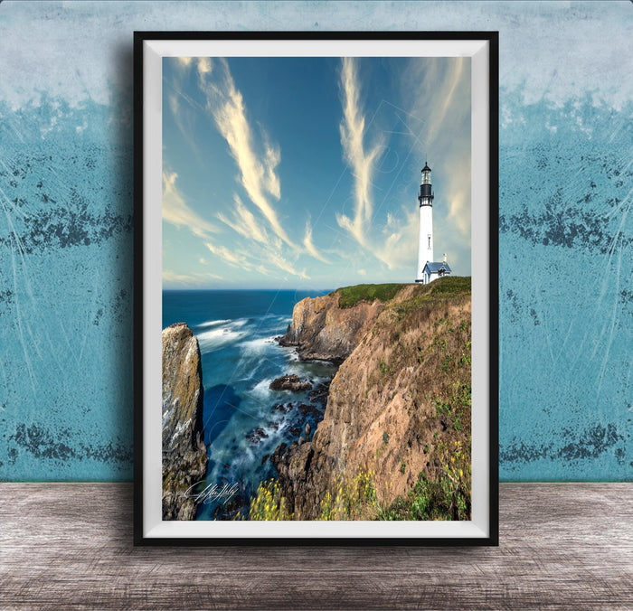 A framed photograph of a lighthouse on a cliff overlooking the ocean, with a blue sky and wispy clouds in the background.