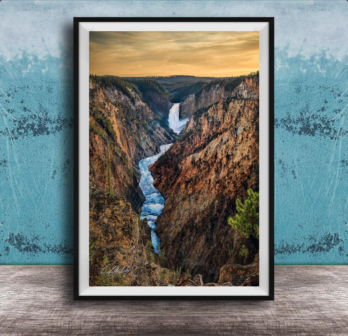 A framed photograph of a breathtaking waterfall cascading down a steep, rocky cliff face, with a vibrant sky in the background.