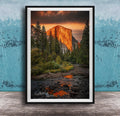 a breathtaking view of a mountain range at sunset, with the sun's warm glow illuminating the peaks and casting a vibrant orange and red hue across the sky. The foreground features a river flowing through the landscape, with rocks and trees lining its banks. The overall composition is visually striking and evokes a sense of tranquility and natural beauty.