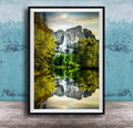 A framed photograph of a serene landscape with a waterfall cascading down a rocky cliff, surrounded by lush green trees and reflected in a calm lake below.