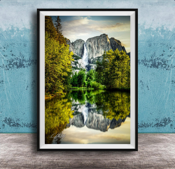 A framed photograph of a serene landscape with a waterfall cascading down a rocky cliff, surrounded by lush green trees and reflected in a calm lake below.