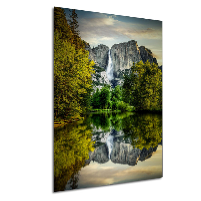 a serene landscape with a large waterfall cascading down a rocky cliff, surrounded by lush green trees and reflected in a calm lake below.