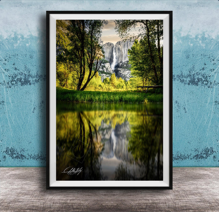 A framed photograph of a serene landscape with a waterfall reflected in a calm lake, surrounded by lush greenery and trees.