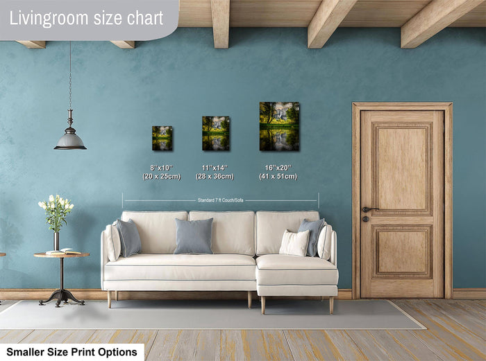 a living room with a white sofa and a wooden door. There are three framed pictures of landscapes displayed on the wall, each with a different size and height. The wall is painted in a light blue color, and there is a lamp hanging from the ceiling. The living room appears to be well-decorated and spacious.