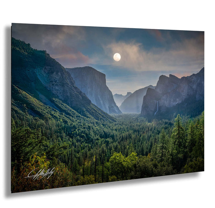 a breathtaking mountainous landscape with a full moon illuminating the scene. The mountains are covered in lush green trees, creating a serene and tranquil atmosphere. The sky above is a beautiful shade of blue, dotted with wispy clouds. The full moon casts a soft, ethereal light over the scene, enhancing the overall beauty of the landscape.
