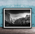 A black and white photograph of a mountainous landscape, with dramatic clouds and a waterfall in the foreground.