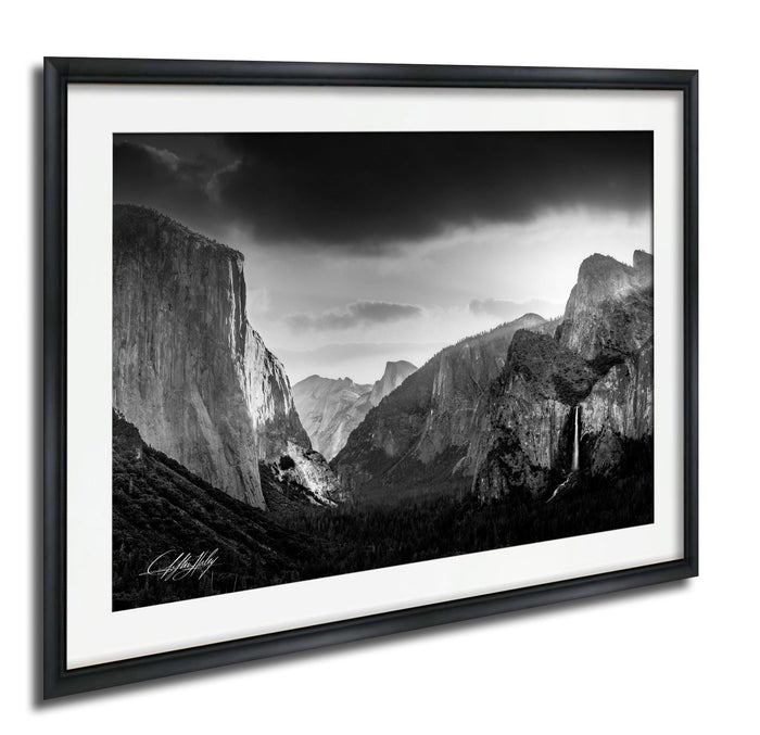 A black and white photograph of the majestic Yosemite Valley, with towering cliffs and a dramatic sky in the background.