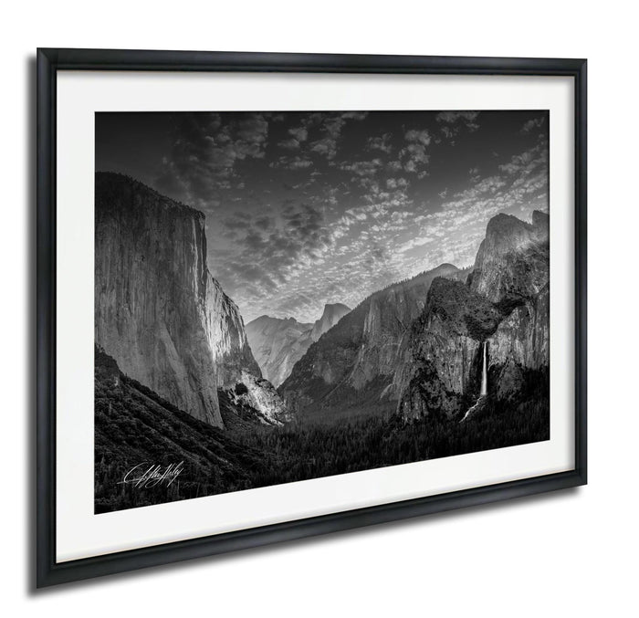 A black and white photograph of the majestic Yosemite Valley, showcasing the towering granite cliffs, the cascading waterfall, and the lush forests below.